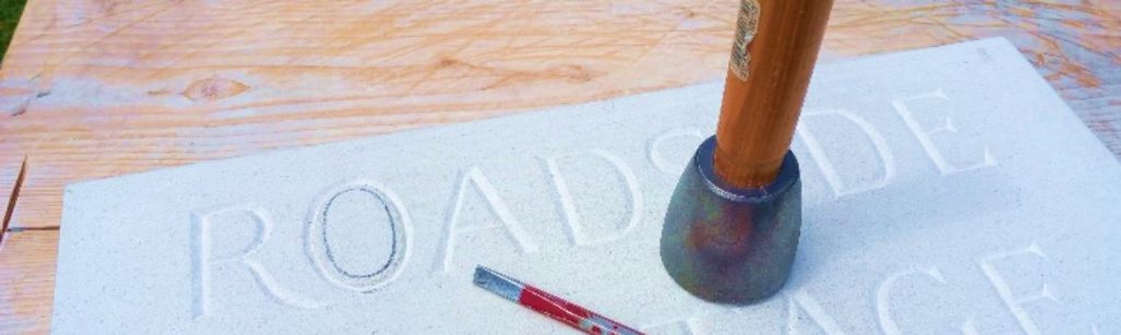 hammer and chisel resting on carved stone - close up of a house sign - v incised stone letter carving done by hand